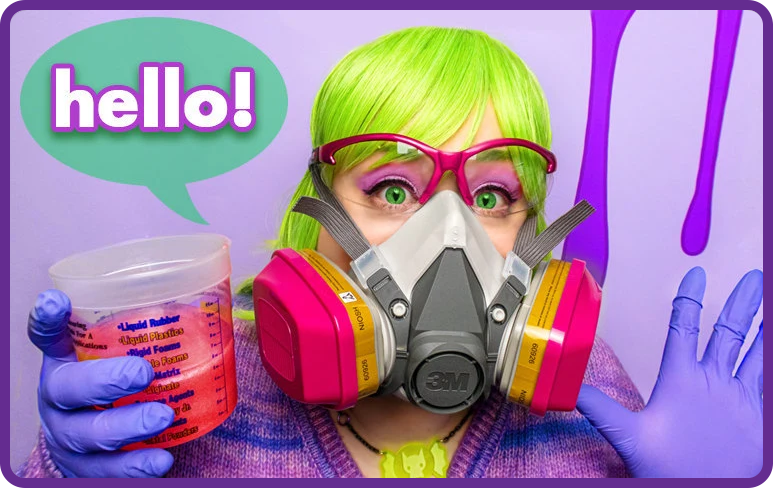A woman with neon green hair wearing safety glasses and a respirator mask holding a vial of resin. A speech bubble reads: Hello!